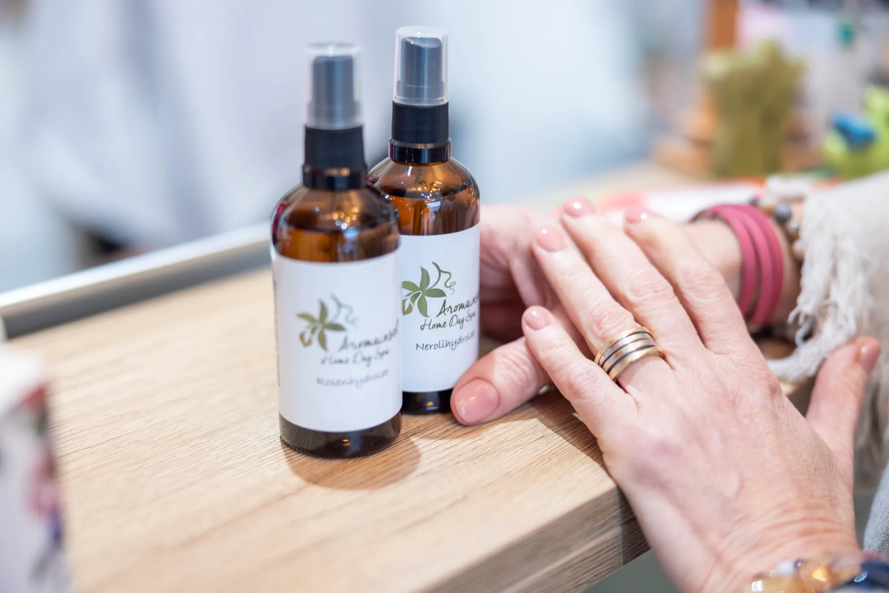 Kaksi Aromainselin tuoksusuihketta puutasolla, vieressä asiakkaan kädet